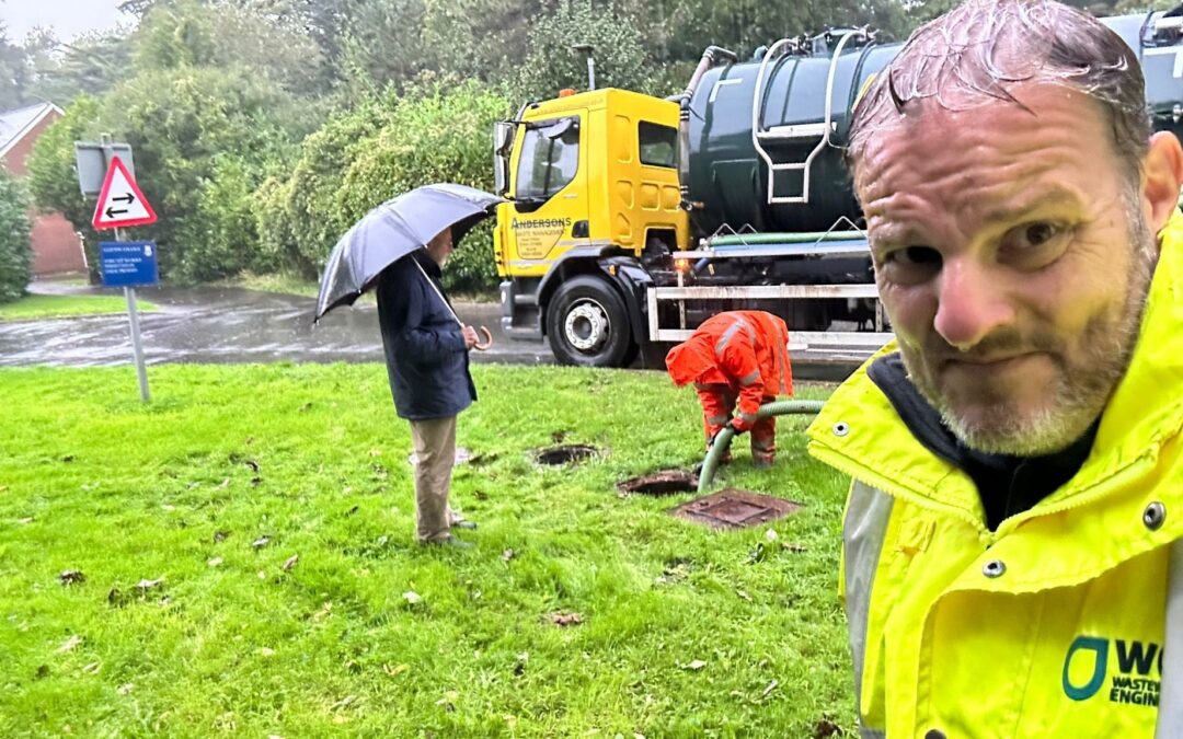 A photo of a WCI engineer and a drainage engineer emptying a sewage treatment system in the pouring rain
