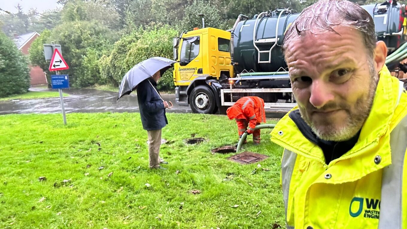 A photo of a WCI engineer and a drainage engineer emptying a sewage treatment system in the pouring rain