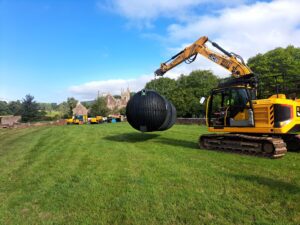 A large sewage treatment plant tank being lifted by a JCB digger during an installation project