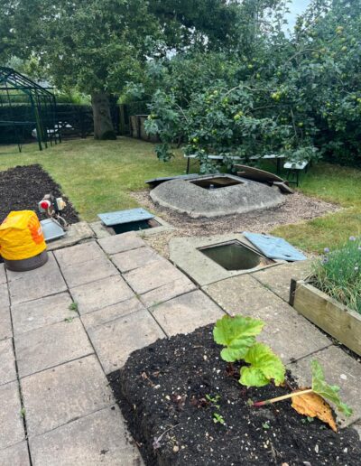 A photo of a garden with paving slabs and flower beds and an aged sewage treatment plant
