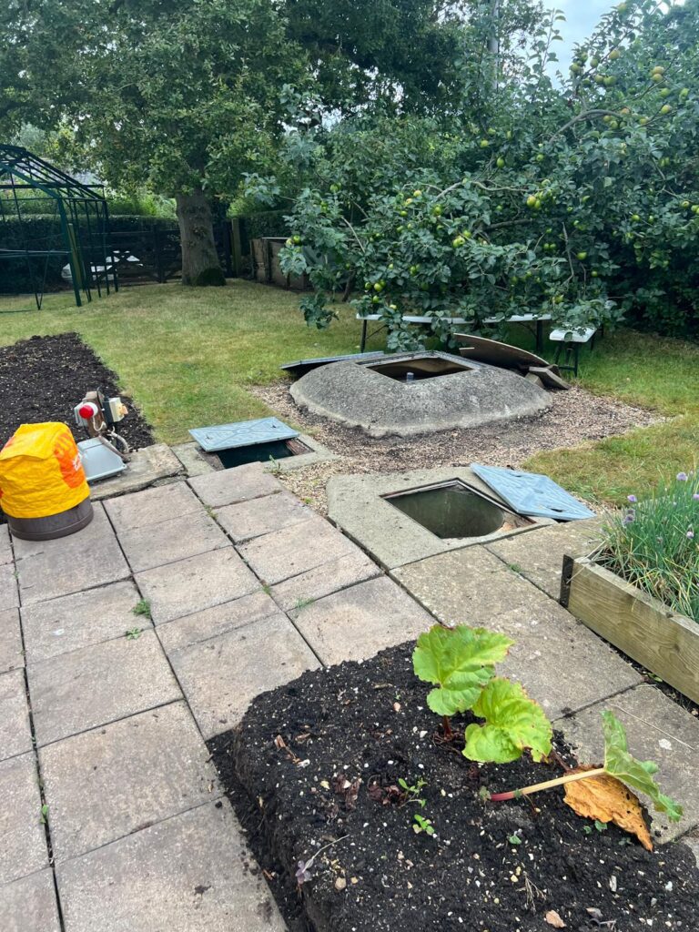 A photo of a garden with paving slabs and flower beds and an aged sewage treatment plant