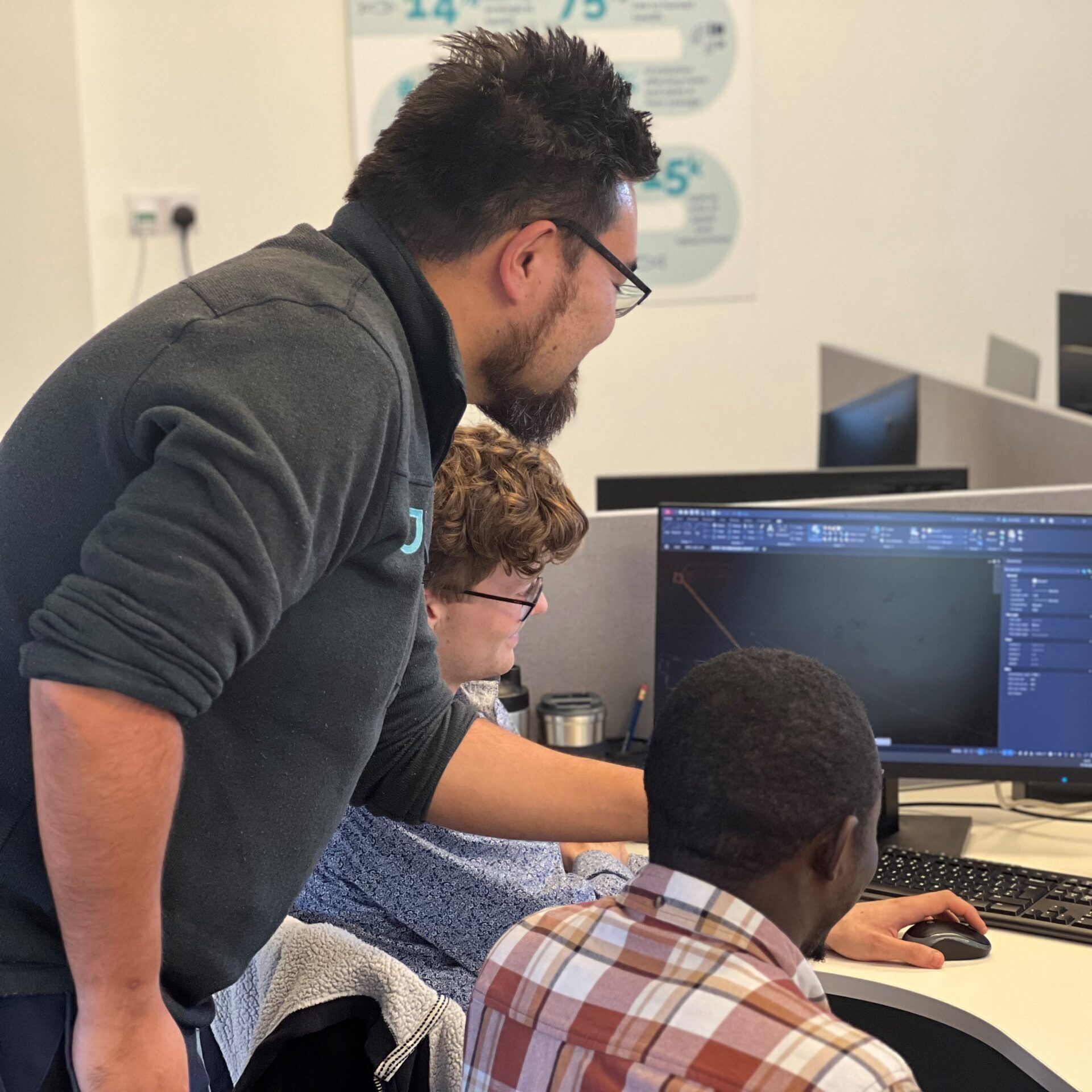 Picture of three engineers gathered around a computer screen discussing an engineering project